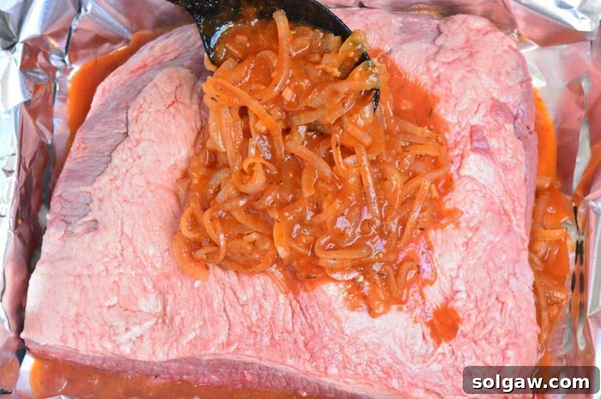 pouring French onion sauce over the uncooked brisket in the foil in the roasting pan.