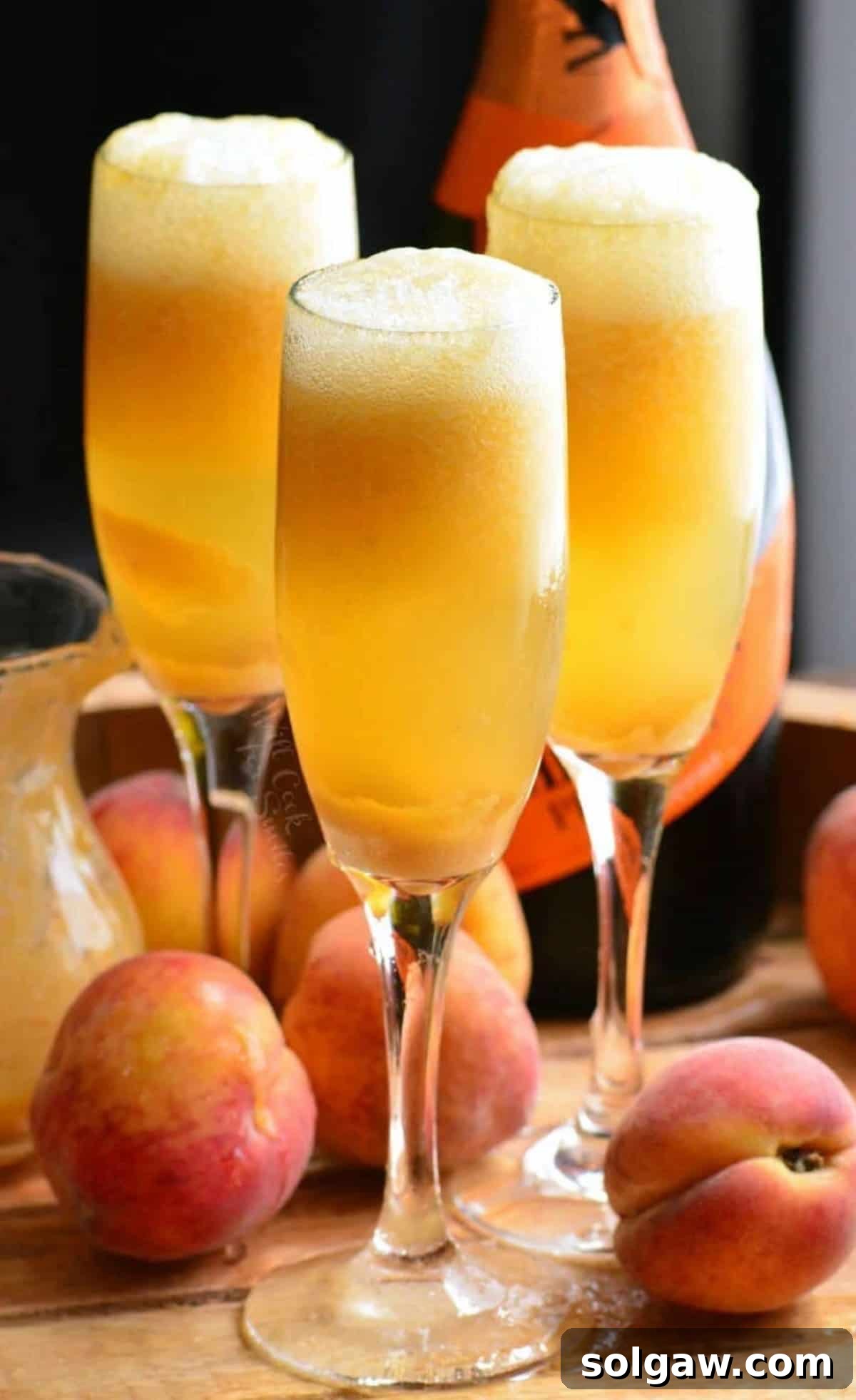 Three tall champagne glasses filled with vibrant orange peach cocktails and a bottle of Prosecco in the background, ready to be enjoyed.