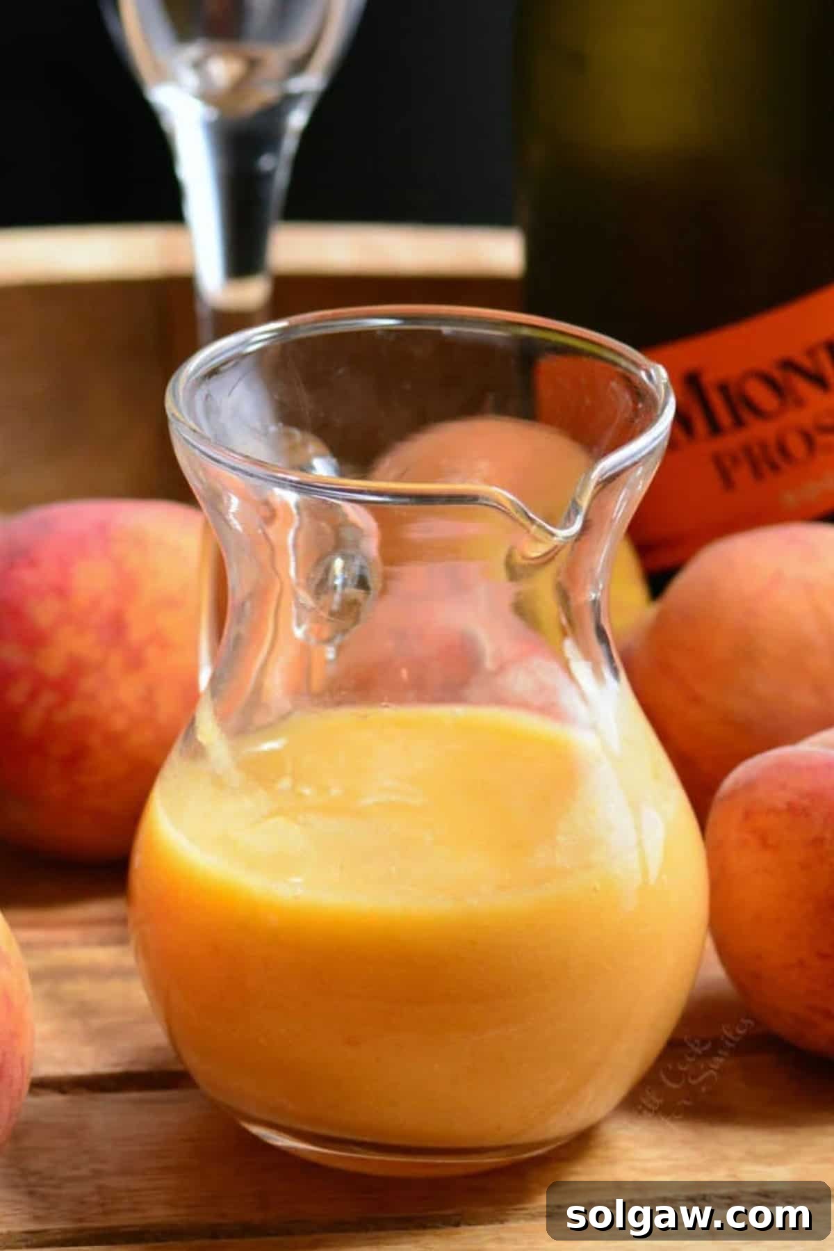 A clear glass pitcher half-filled with a smooth, golden peach puree, showcasing its rich texture and readiness for cocktails.