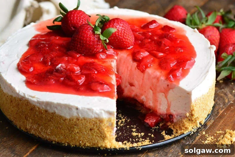 A slice of No-Bake Strawberry Cheesecake on a plate, with the rest of the cake on a wooden table, surrounded by fresh strawberries.