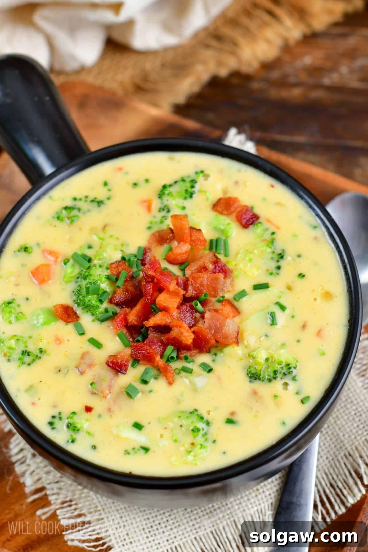 A steaming bowl of homemade Bacon Broccoli Cheese Soup, garnished with crispy bacon pieces and fresh chives, with a spoon ready for tasting.