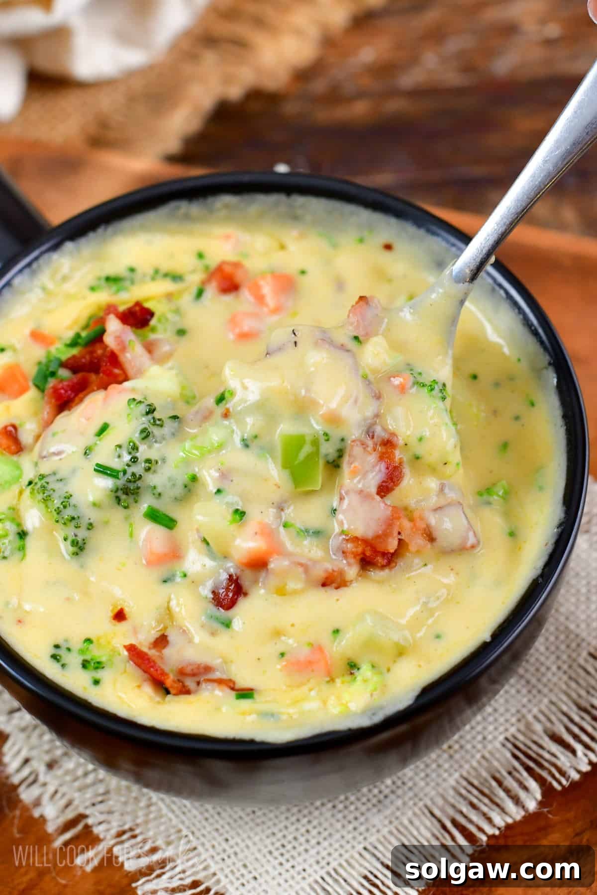 A spoonful of creamy Bacon Broccoli Cheese Soup being lifted from a bowl, showing the rich texture and delicious ingredients.