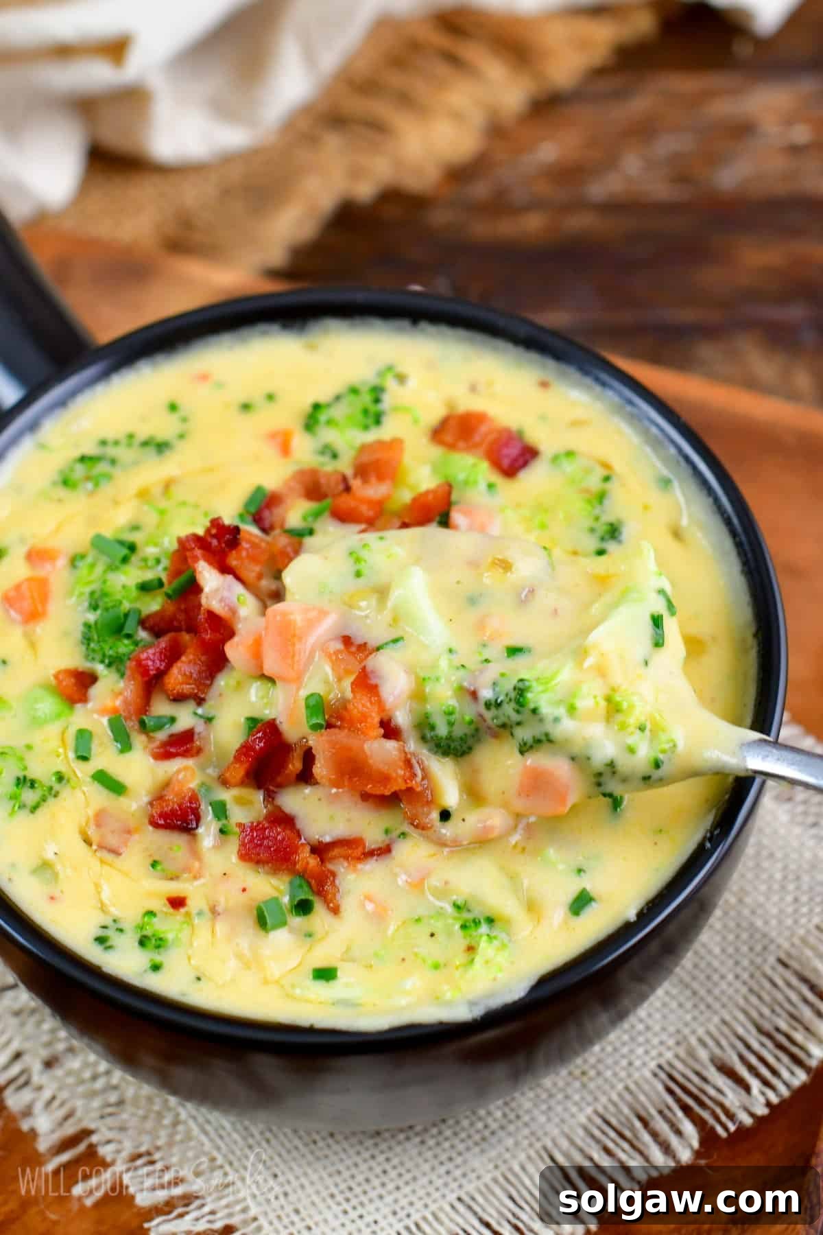 A bowl of creamy Bacon Broccoli Cheese Soup being scooped with a spoon, highlighting the rich texture and ingredients.
