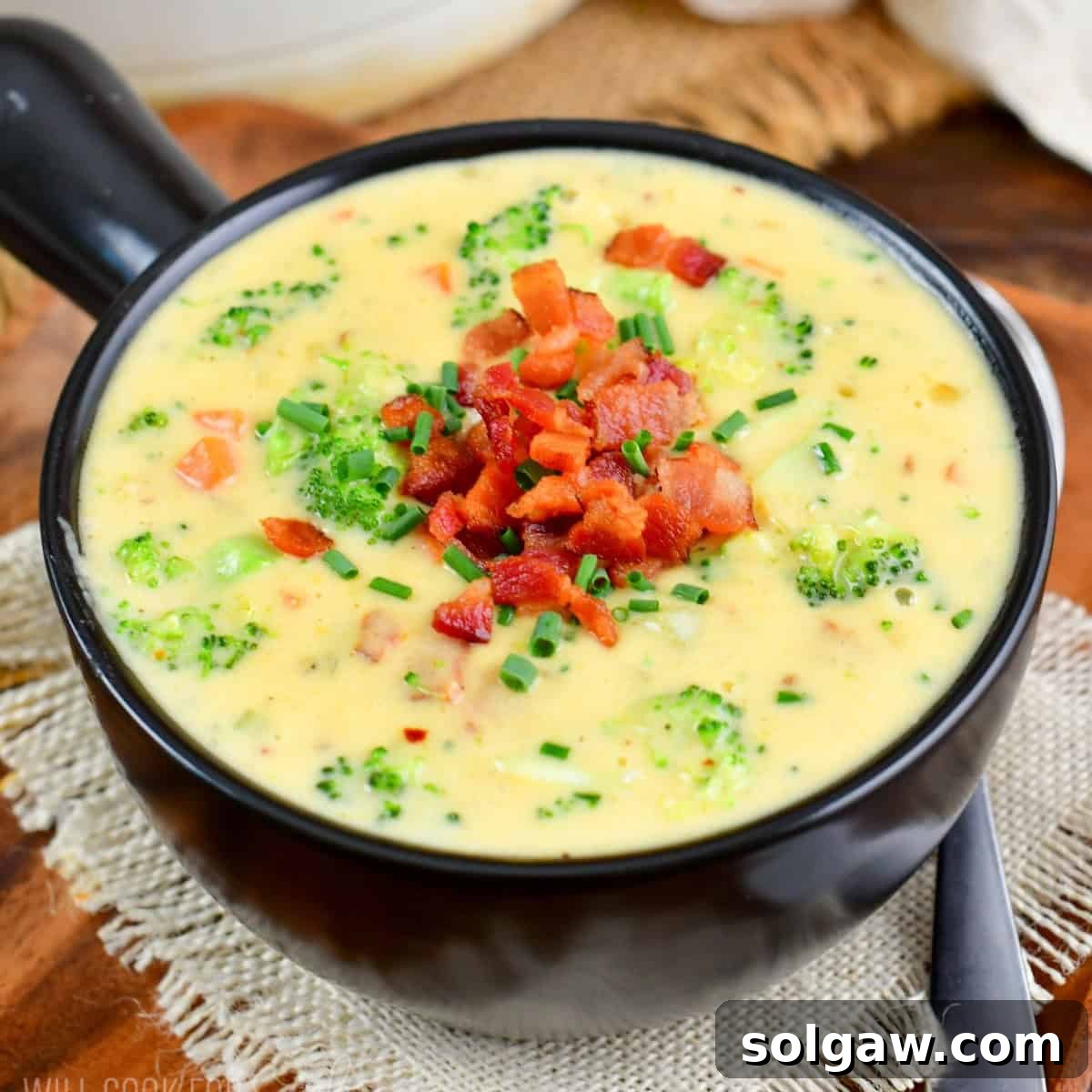 A black bowl filled with creamy bacon broccoli cheese soup, garnished with crispy bacon and fresh chives.