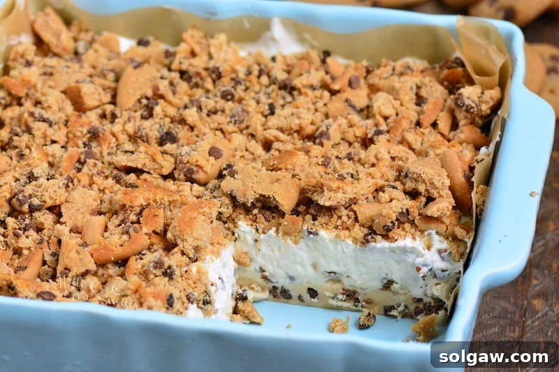 A Cookie Dough No Bake Cheesecake in a square pan with one slice already removed, showing the layered structure.