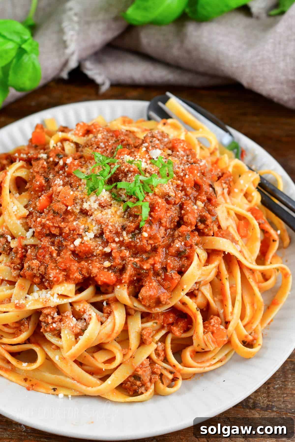 Fettuccine mixed and topped with rich, slow-simmered Bolognese sauce on a plate with a fork, garnished with fresh basil.