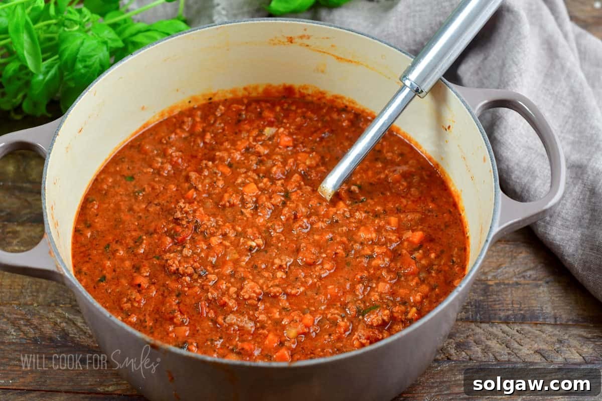 A large pot filled with rich, cooked red Bolognese sauce, with a ladle resting inside, ready to be served or stored.