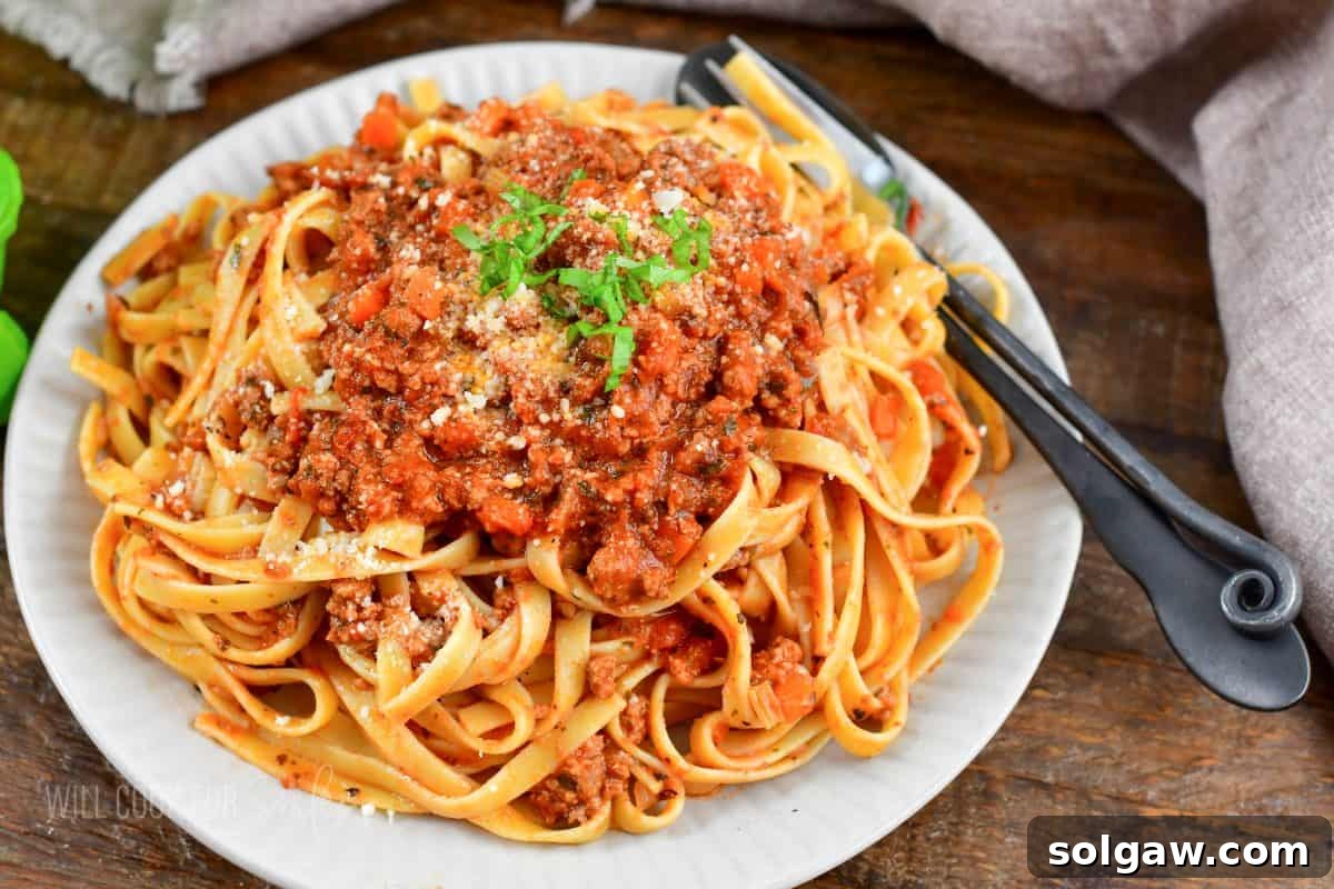 A plate of fettuccine pasta generously topped with rich Bolognese sauce, garnished with grated parmesan cheese and fresh basil leaves, ready to be enjoyed.