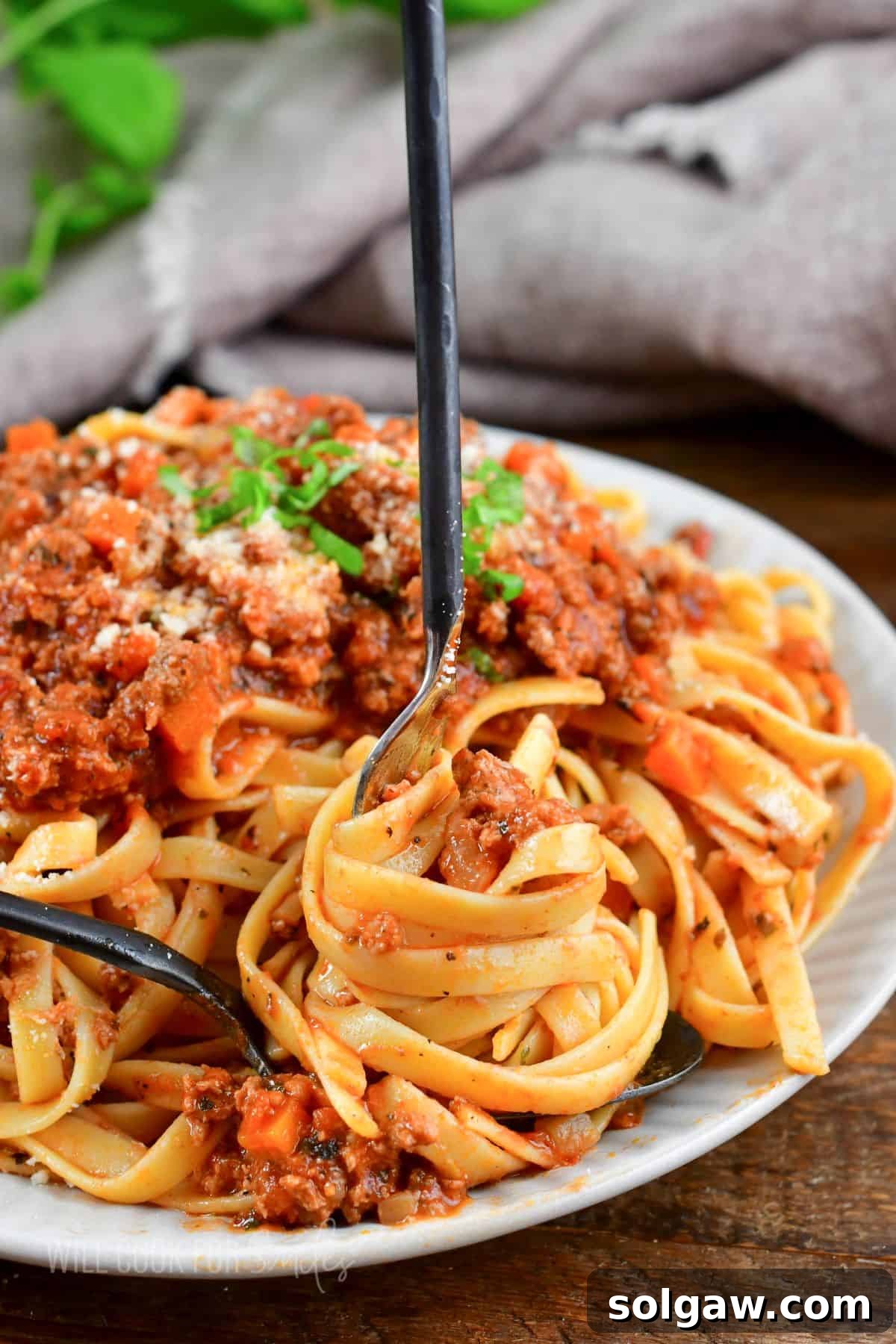 A fork elegantly swirling fettuccine pasta coated in vibrant red meat sauce over a spoon, highlighting the saucy texture.