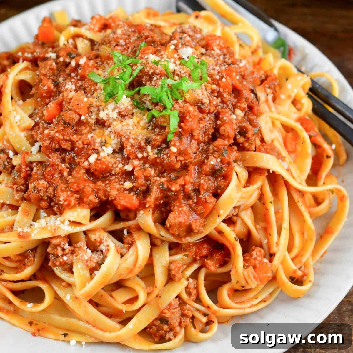 fettuccine pasta mixed and topped with a tomato based meat sauce on a plate.