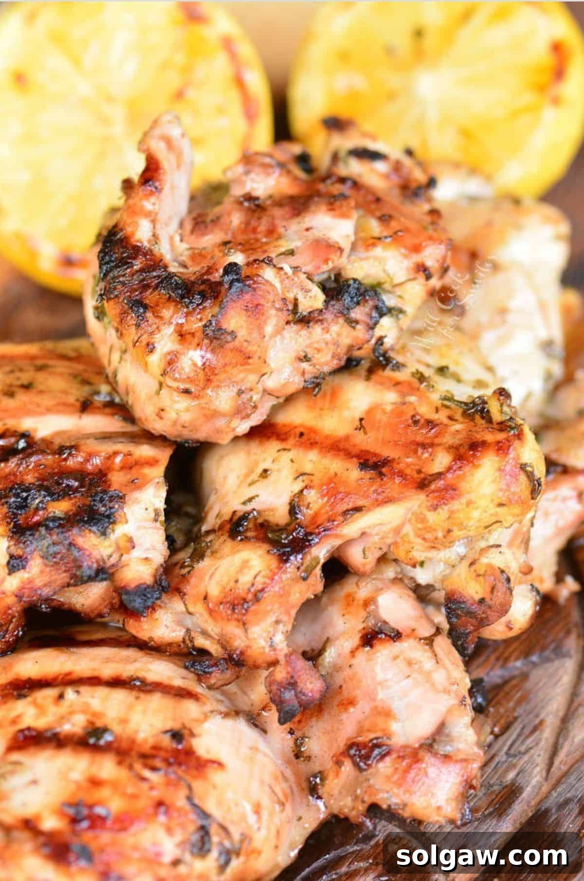grilled marinated Greek chicken thighs on wooden plate with lemon halves.