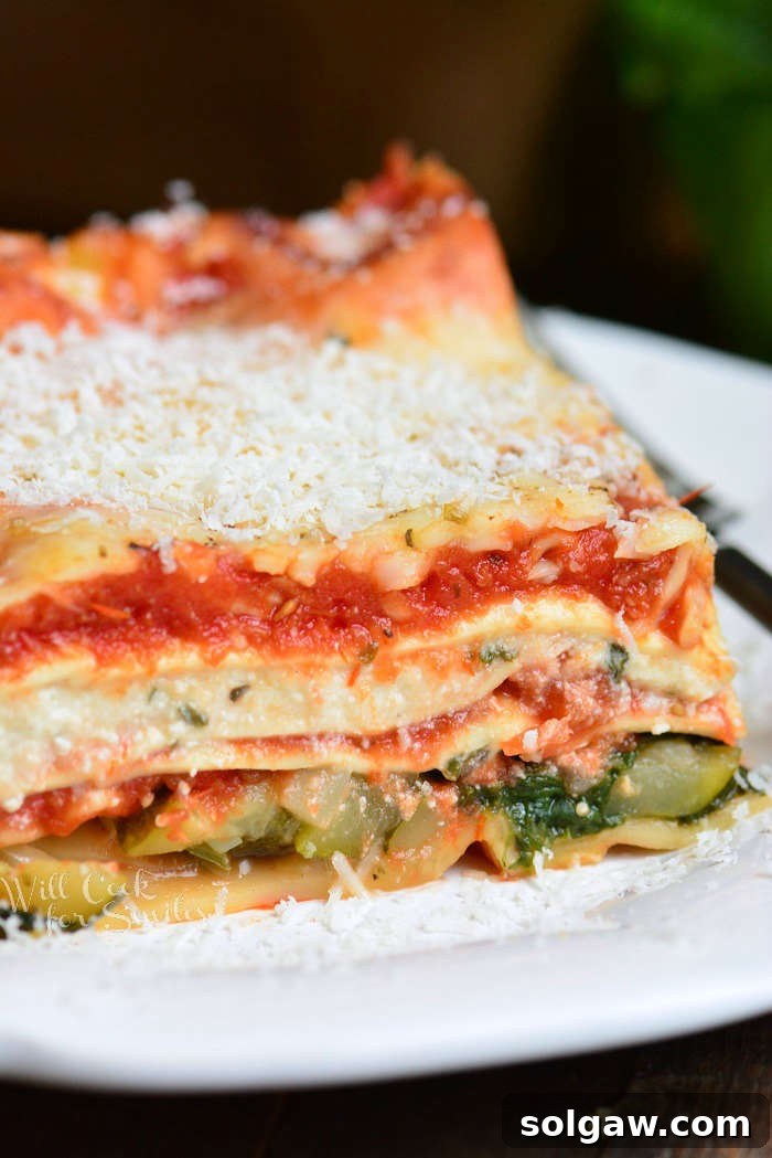 A beautifully layered vegetable lasagna slice on a plate, showcasing vibrant green spinach, yellow zucchini, and creamy ricotta, topped with melted cheese.