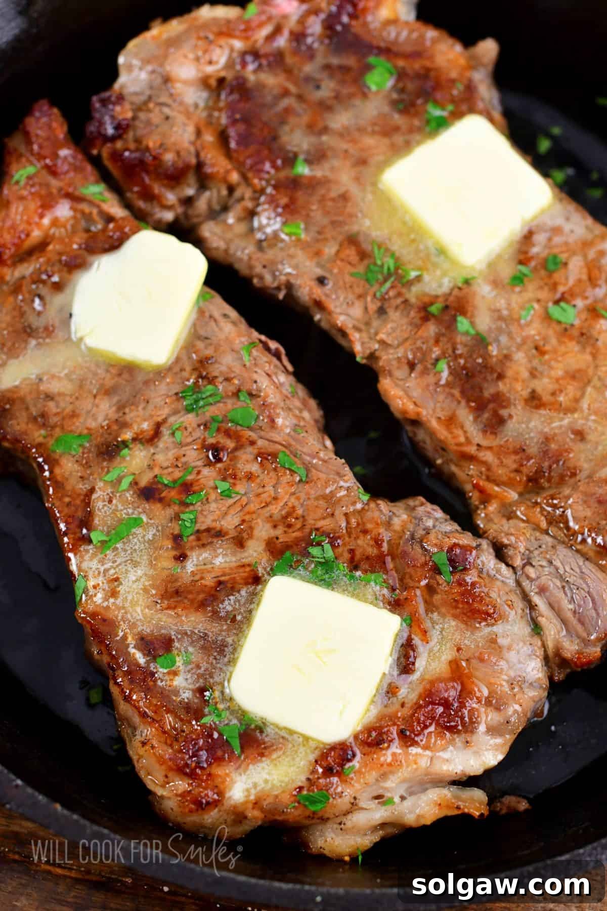 Two perfectly cooked steaks, topped with melting butter and fresh parsley, resting in a cast iron skillet.