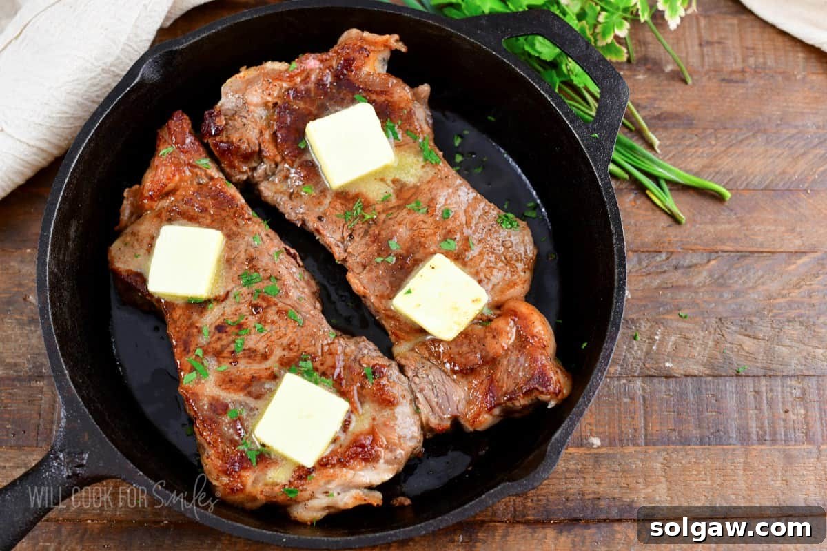 Two perfectly oven-cooked steaks topped with melting butter and fresh parsley, presented in a black cast iron skillet, ready to be served.