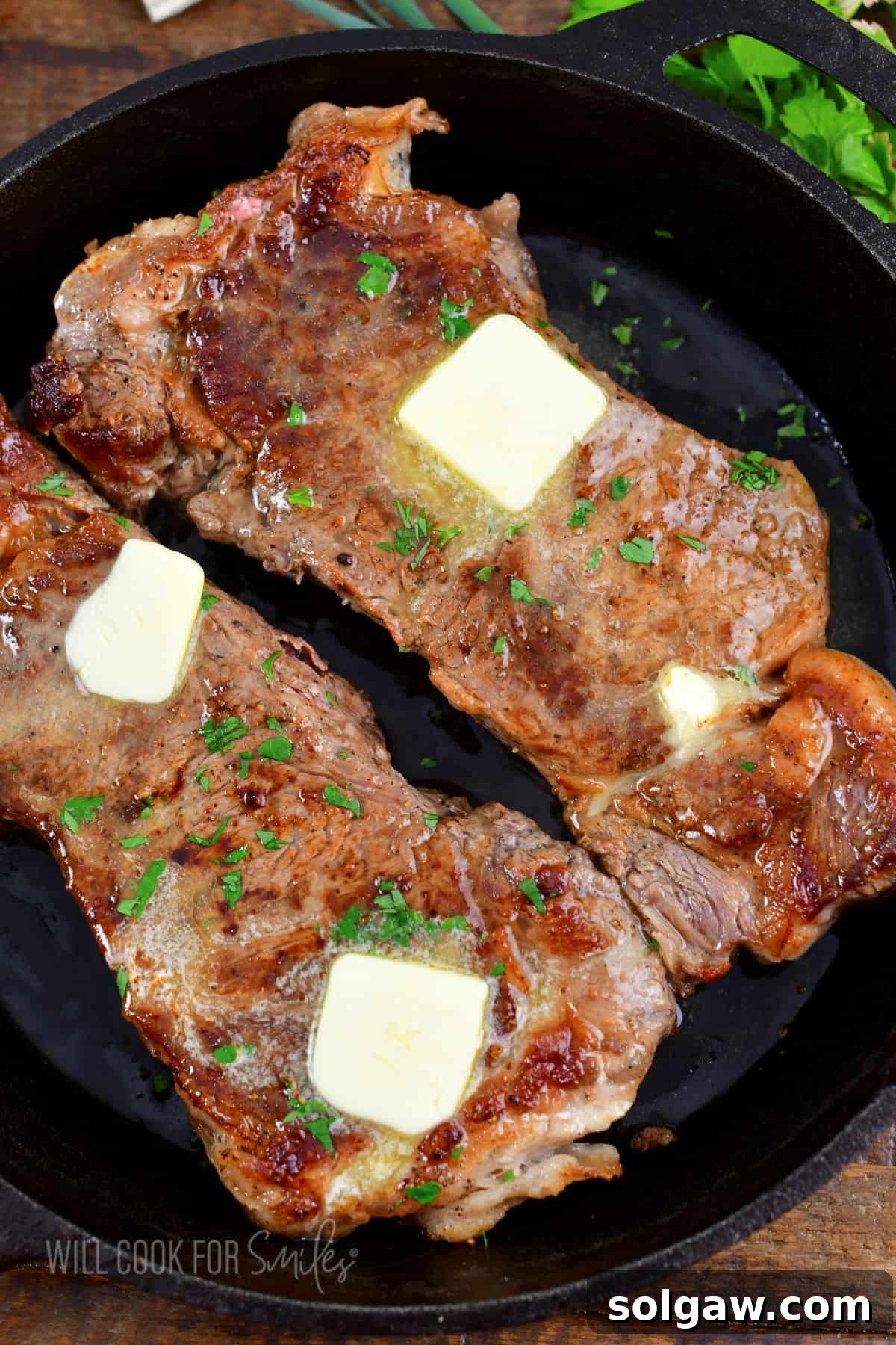 Close-up of butter slices melting gracefully on top of two freshly cooked steaks in a cast iron skillet, enhancing their flavor and sheen.