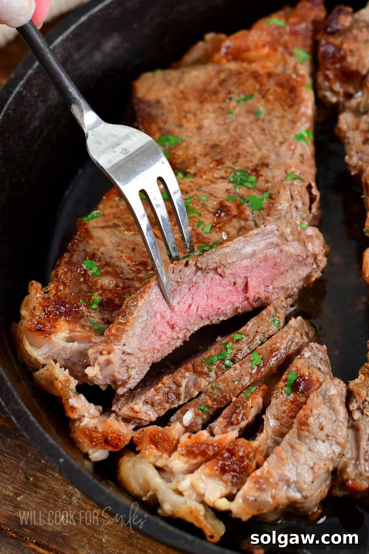 A perfectly sliced steak, revealing an even medium-rare doneness, presented in a skillet with a fork lifting a piece for tasting.