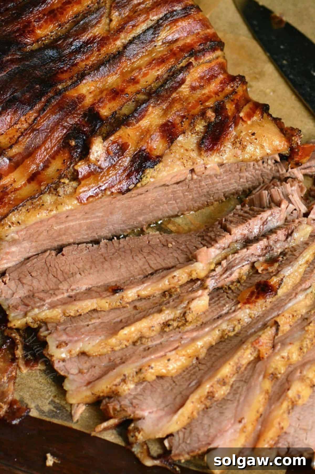sliced bacon wrapped juicy beef brisket on parchment paper.