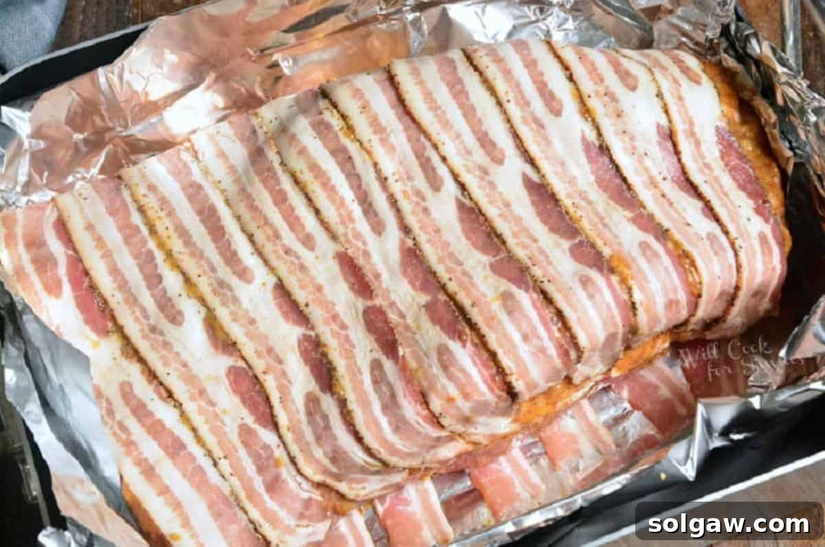 uncooked whole beef brisket seasoned and wrapped in bacon in aluminum paper in roasting pan.