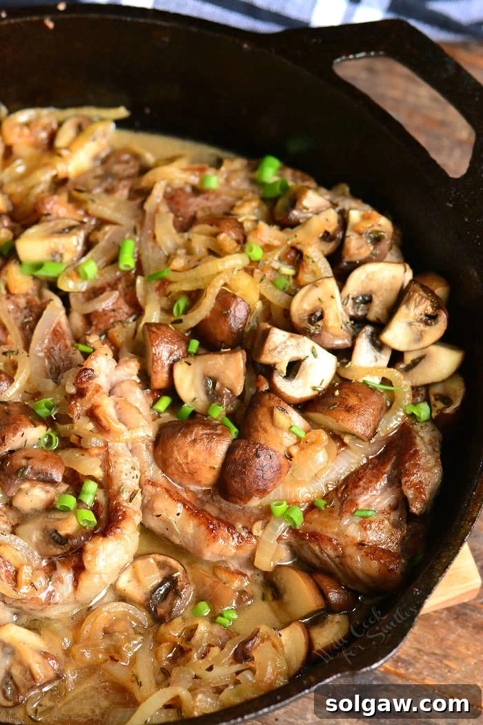 Two perfectly seared rib eye steaks in a skillet, richly topped with glistening sauce, sautéed mushrooms, and caramelized onions.