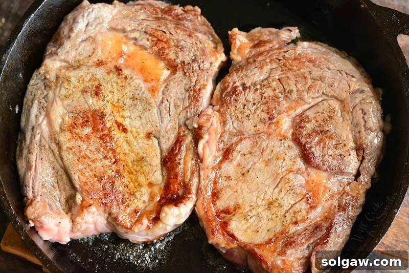 Two succulent rib eye steaks sizzling and searing to a perfect crust in a hot cast iron skillet.