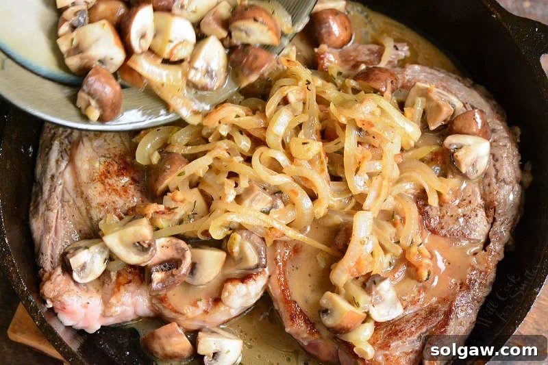 The tantalizing sight of sautéed mushrooms and onions being generously added over perfectly cooked rib eye steaks in a skillet, ready for serving.