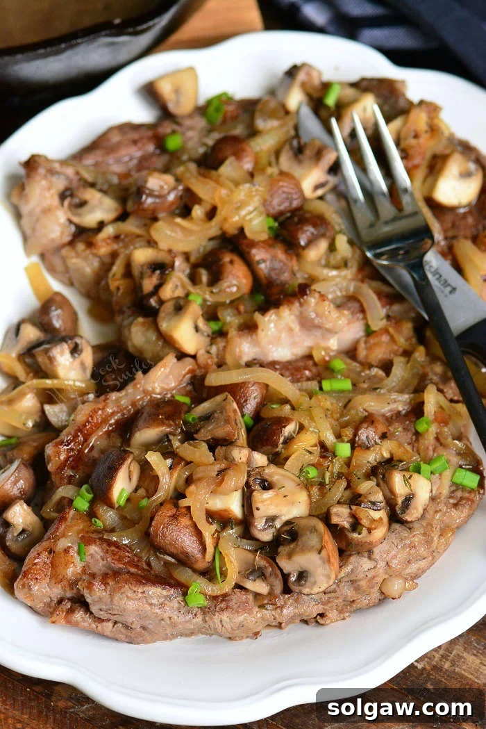 A beautifully plated rib eye steak, crowned with sautéed mushrooms and onions, with a fork poised for a delicious bite.