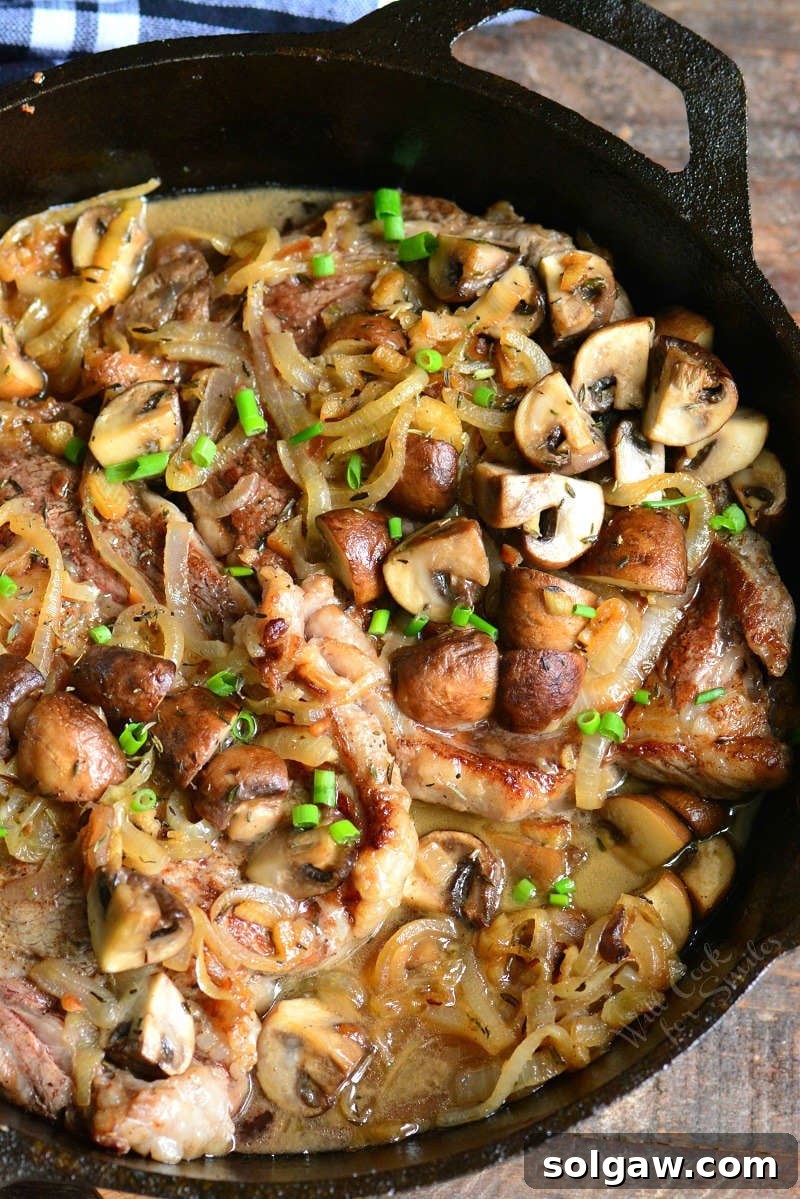 A round image of a cooked rib eye steak with mushrooms and onions on a plate.