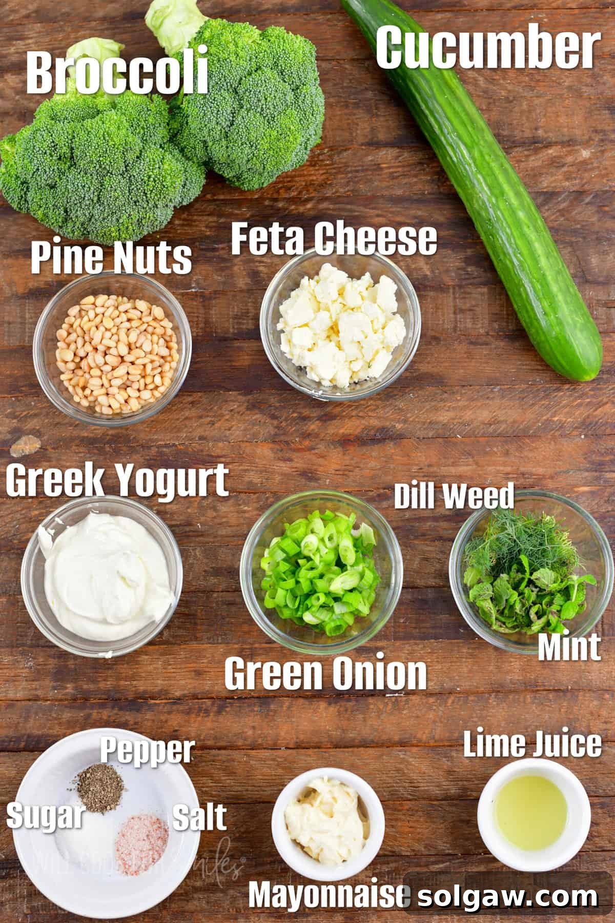 Labeled ingredients for broccoli cucumber salad are placed on a wooden surface. 