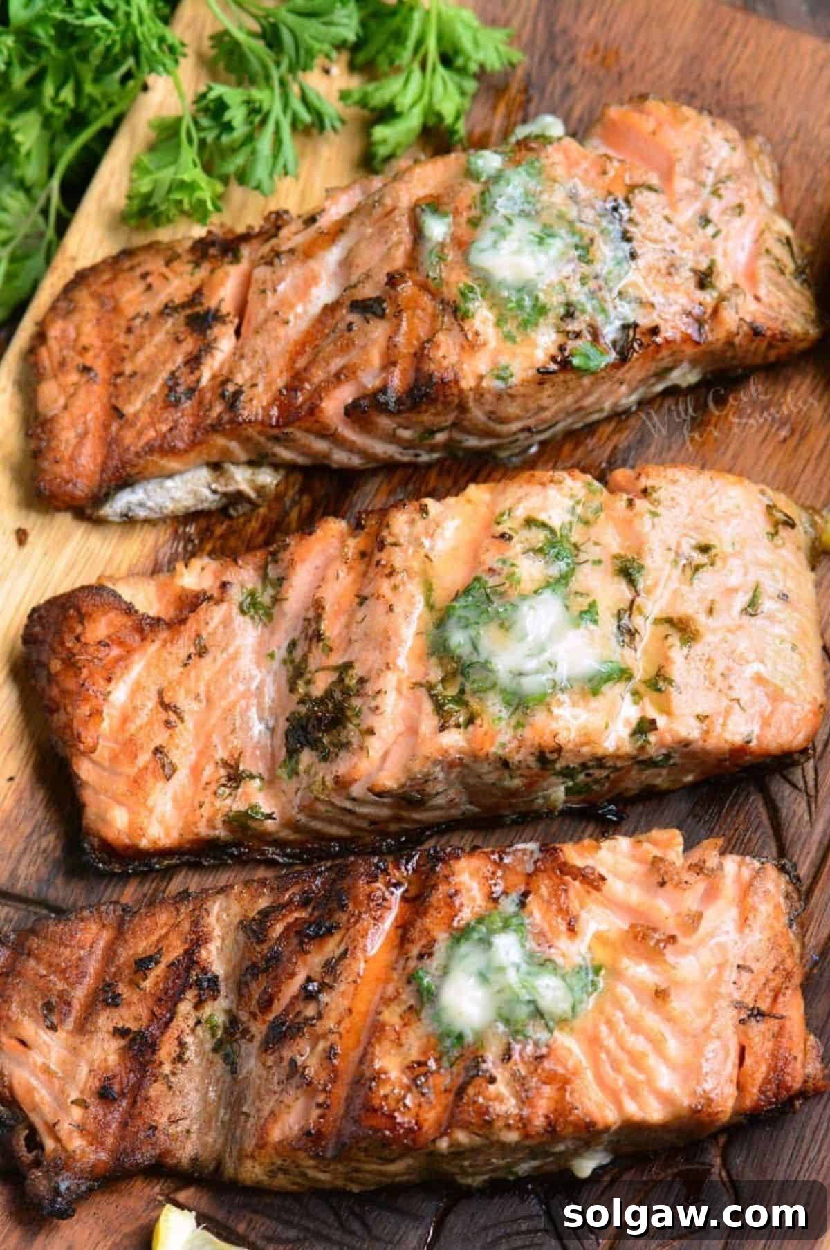 three grilled salmon filets topped with garlic butter on the wooden plate.