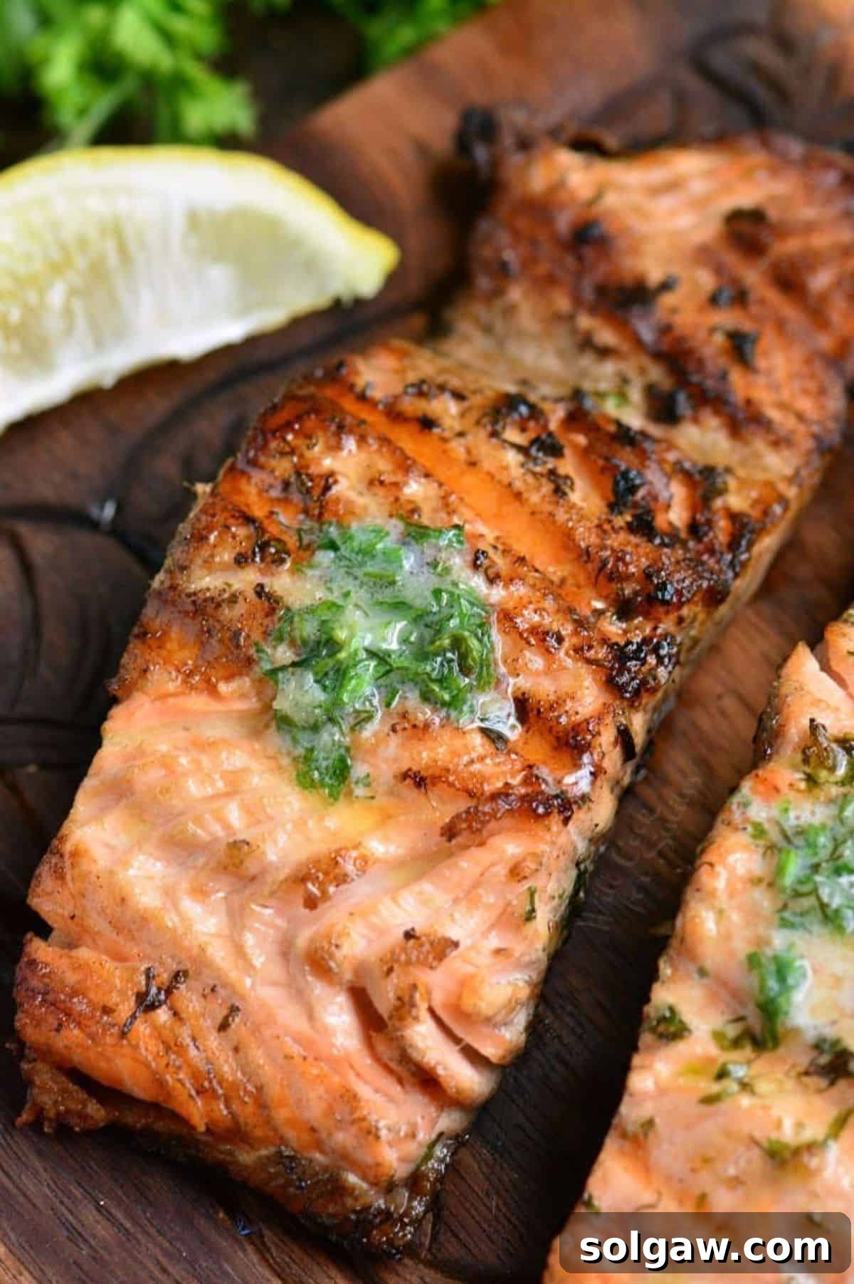 a grilled salmon filet topped with melting herb butter and lemon wedge.
