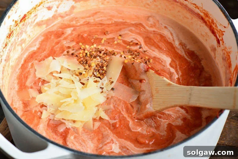A wooden spoon stirring vibrant red vodka sauce ingredients in a stock pot, showing the process of mixing