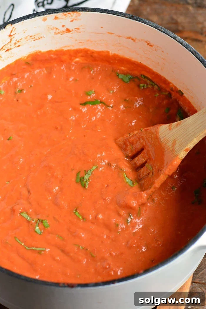 A wooden spoon stirring a pot of creamy red vodka sauce, showing the rich texture and readiness to combine with pasta