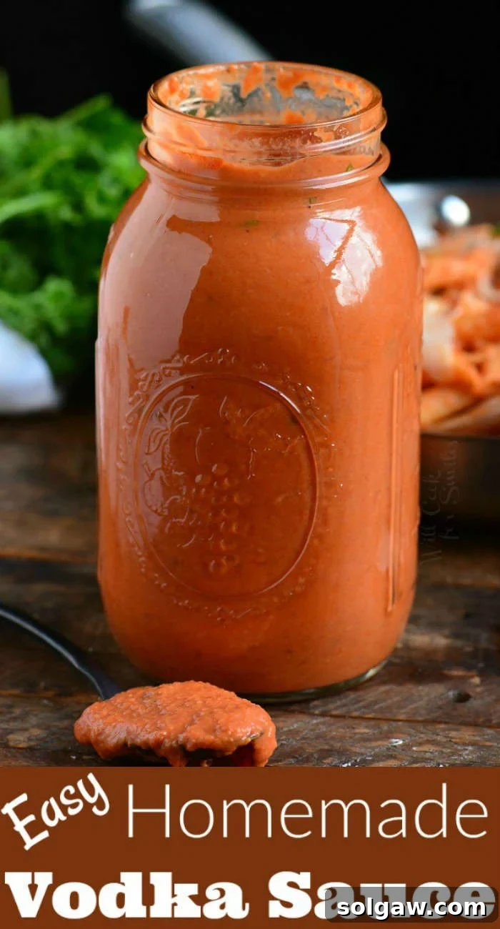 Homemade vodka sauce stored in a clear glass jar, with a spoon taking a scoop, placed on a rustic wood board