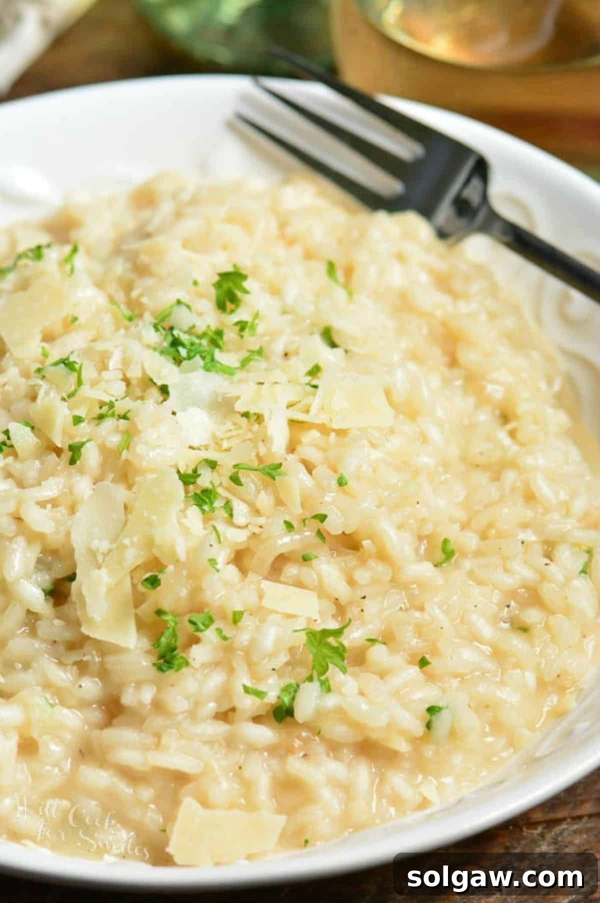 Creamy Grana Rice 9 A bowl of parmesan risotto garnished with fresh cheese and parsley, with a fork beside it.