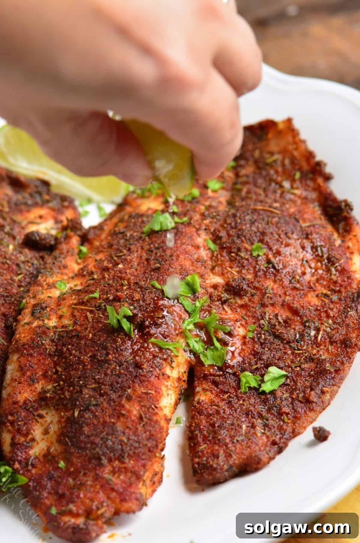 Squeezing lime over cooked blackened tilapia that is on a plate.