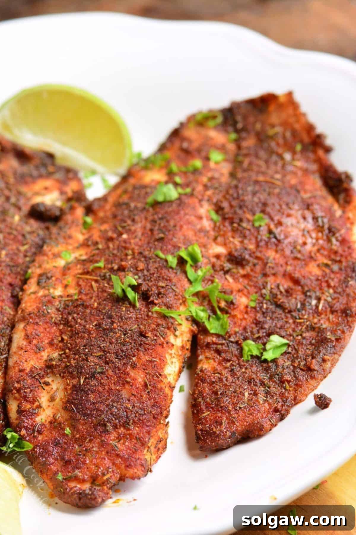 Blackened tilapia on a white plate with a slice of lime.