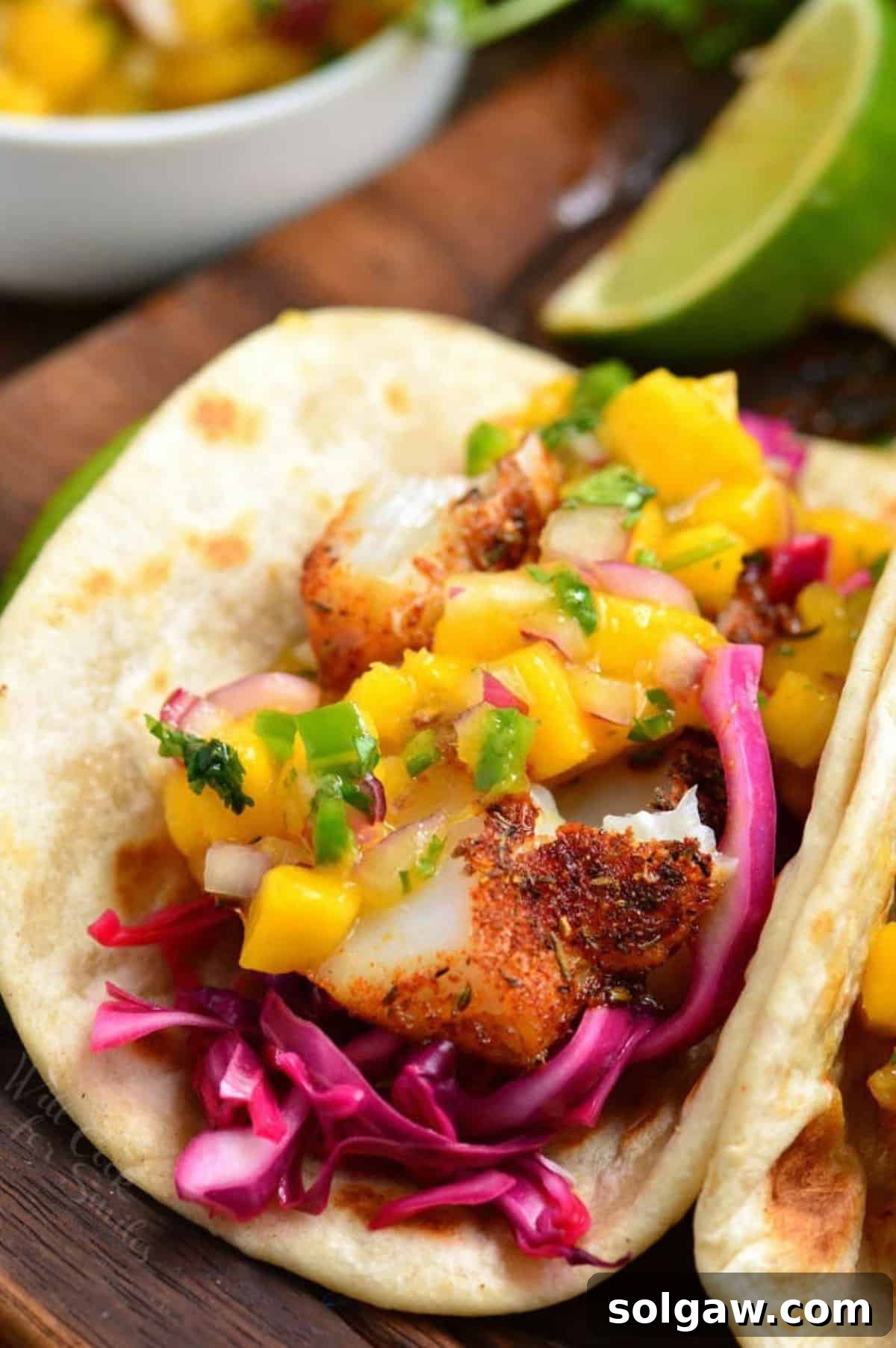 Blackened fish taco with cabbage and mango salsa on a wood surface.