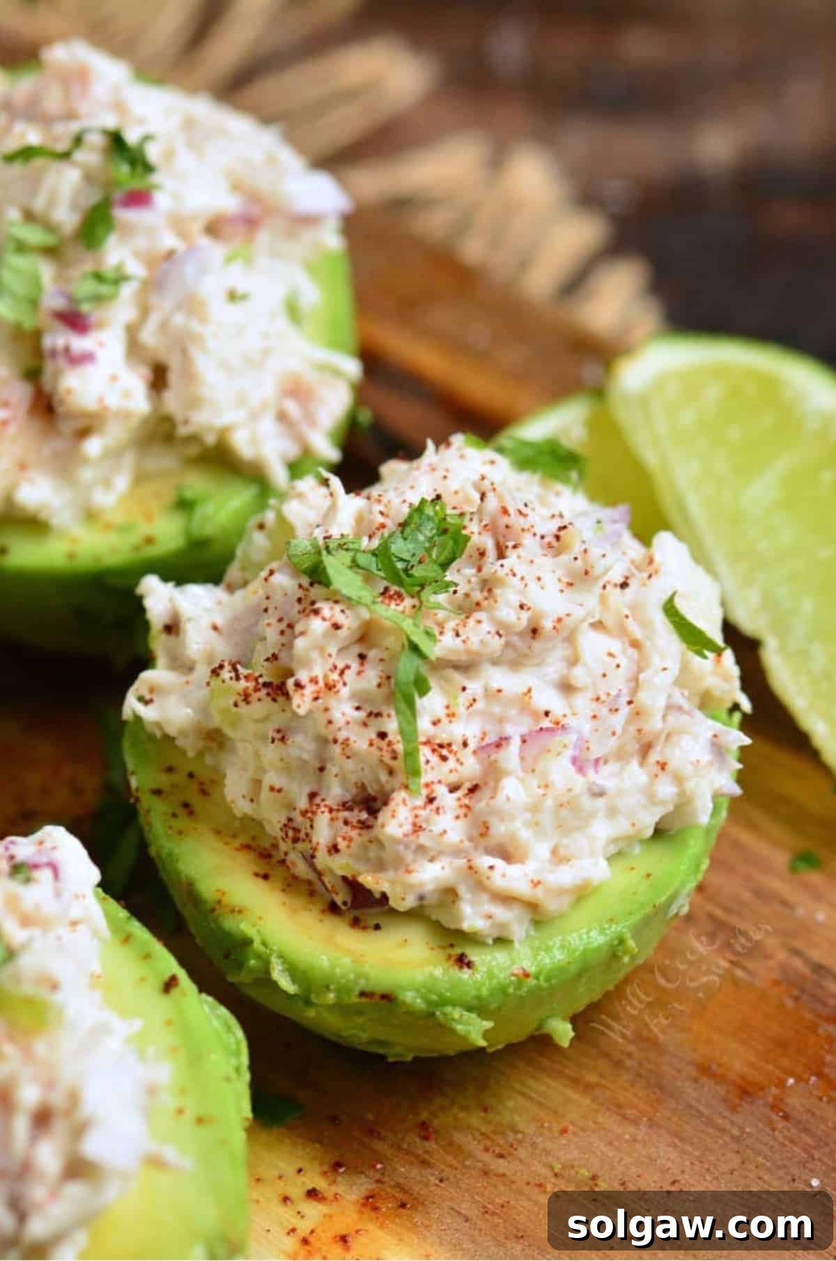 avocado half stuffed with chicken salad and topped with parsley and a lime wedge next to it.