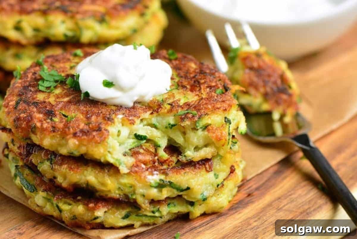 Crispy Zucchini Fritters 7 three zucchini fritters stacked and topped with sour cream with a fork.
