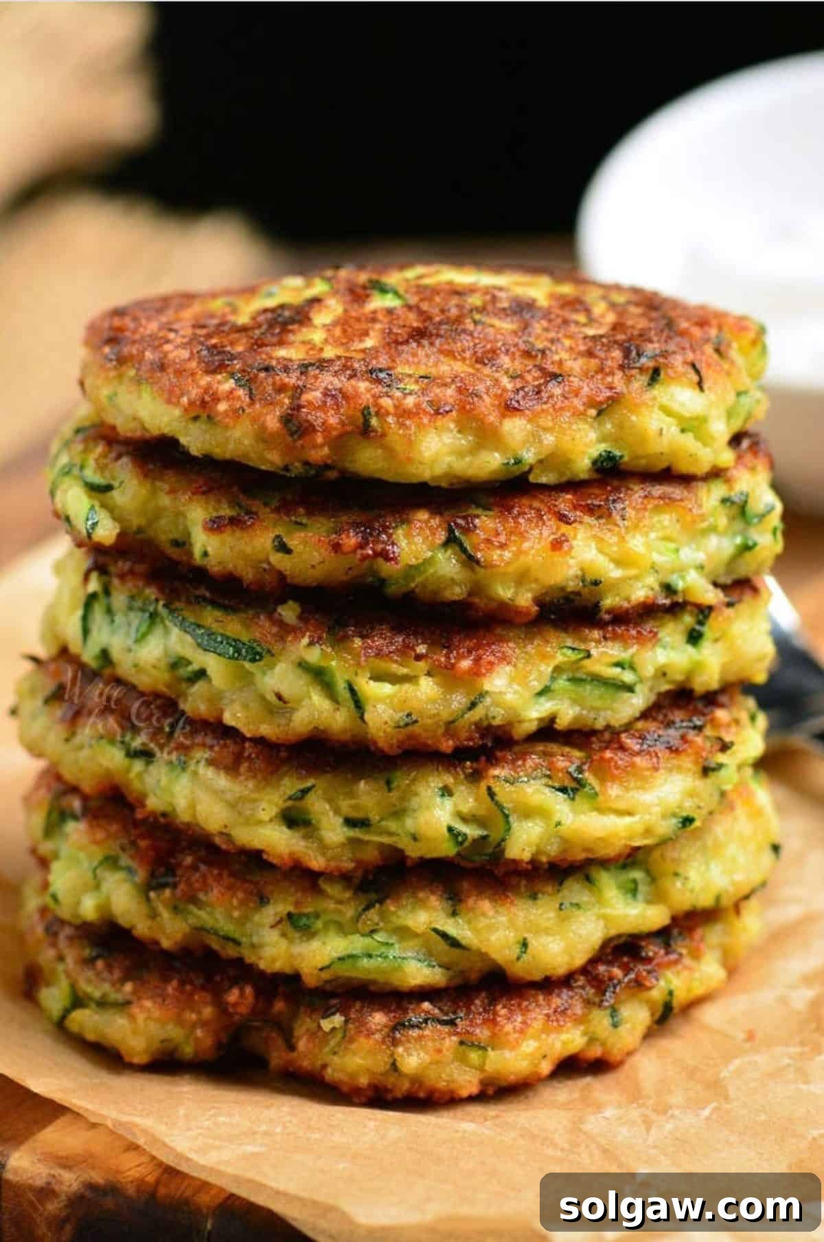 Crispy Zucchini Fritters 8 six zucchini fritters stacked on top of each other on parchment paper.