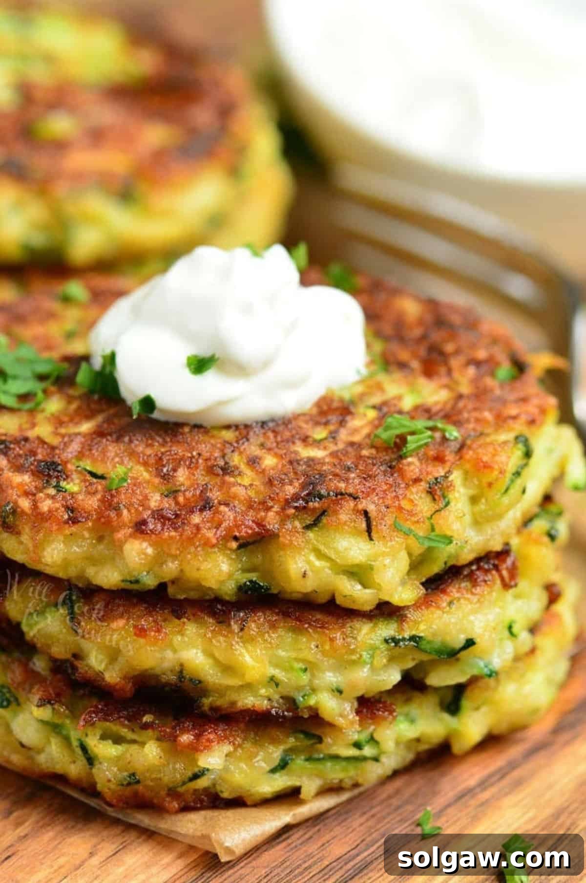Crispy Zucchini Fritters 9 three zucchini fritters stacked and topped with sour cream.