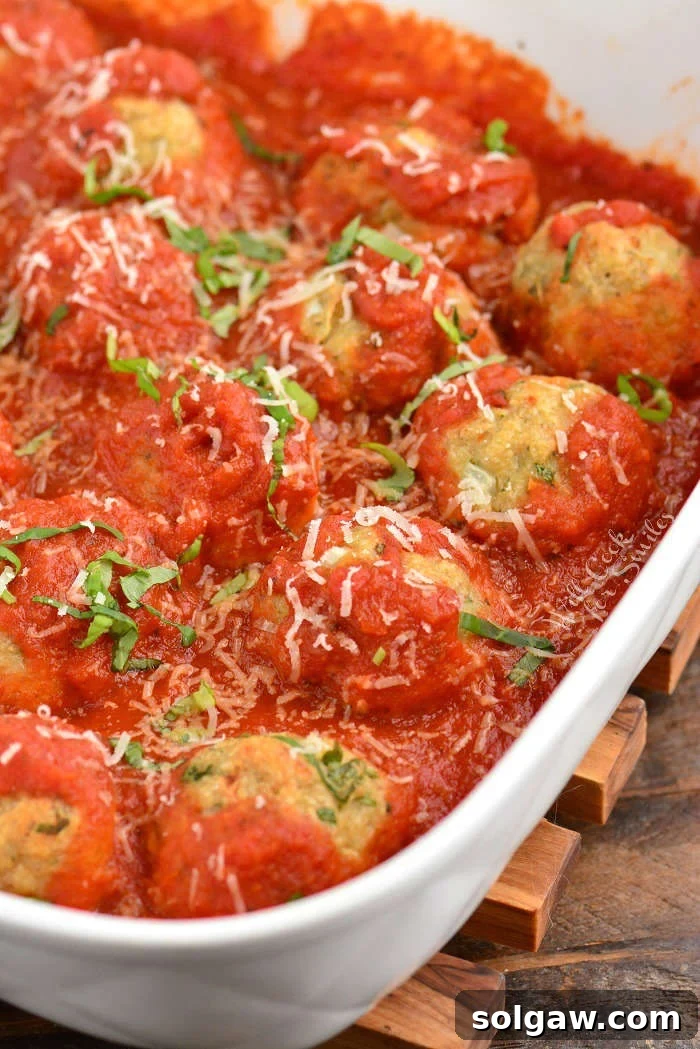 Close-up of baked Italian chicken meatballs in a rich marinara sauce, garnished with fresh basil.