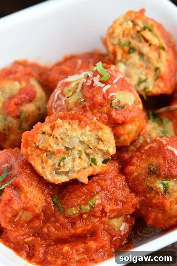 A serving of baked Italian chicken meatballs over pasta with fresh basil and Parmesan.