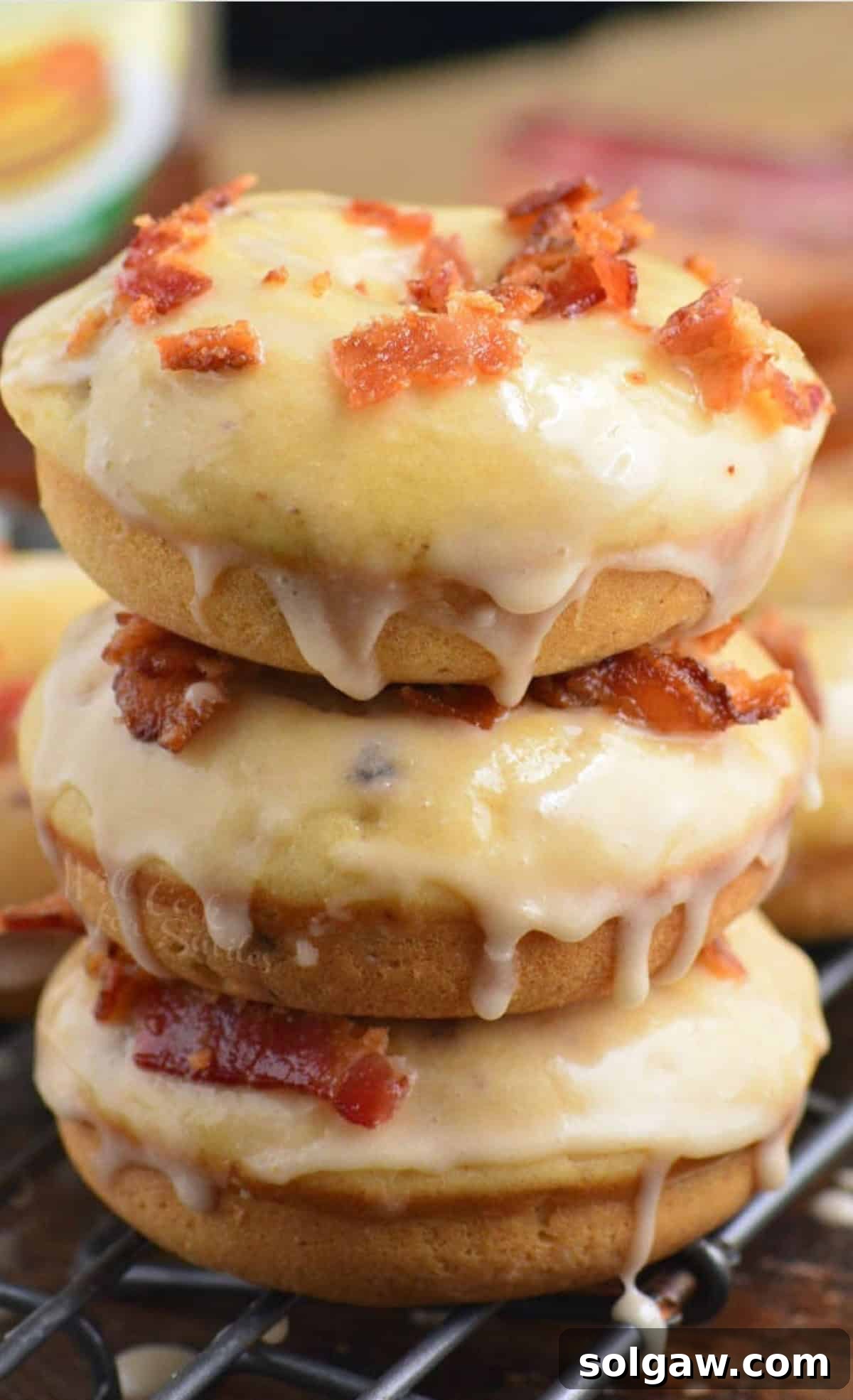 Three maple bacon donuts in a stack on a wire rack, ready to be enjoyed.