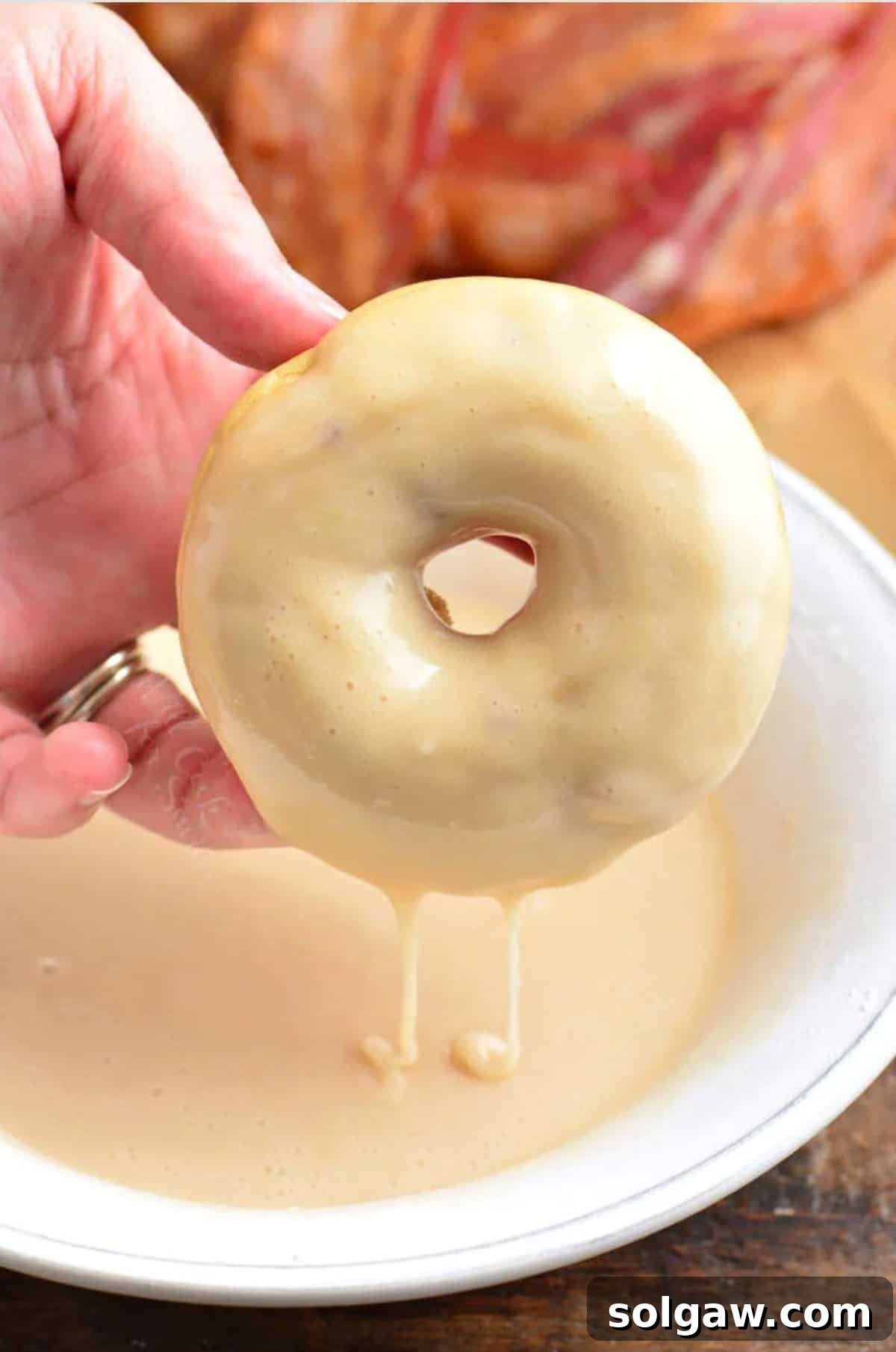 Dipping a maple donut into a bowl of icing, with bacon bits waiting to be sprinkled.