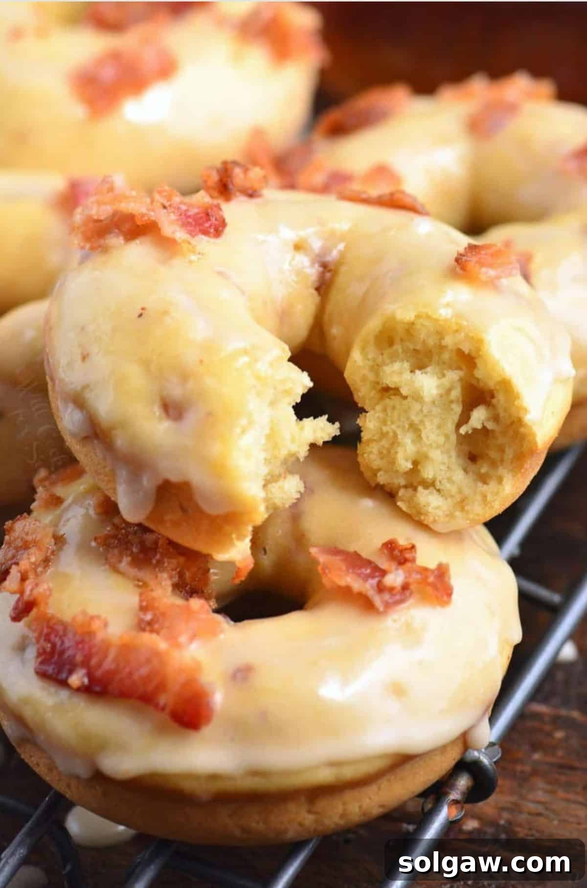 Maple bacon donuts stacked on a wire rack with one broken to reveal the soft interior.