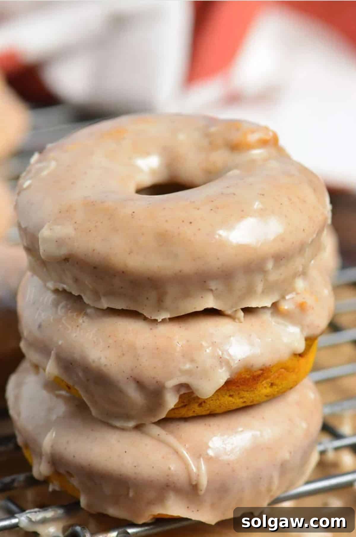 Stacked baked pumpkin donuts on a wire cooling rack, glistening with glaze.