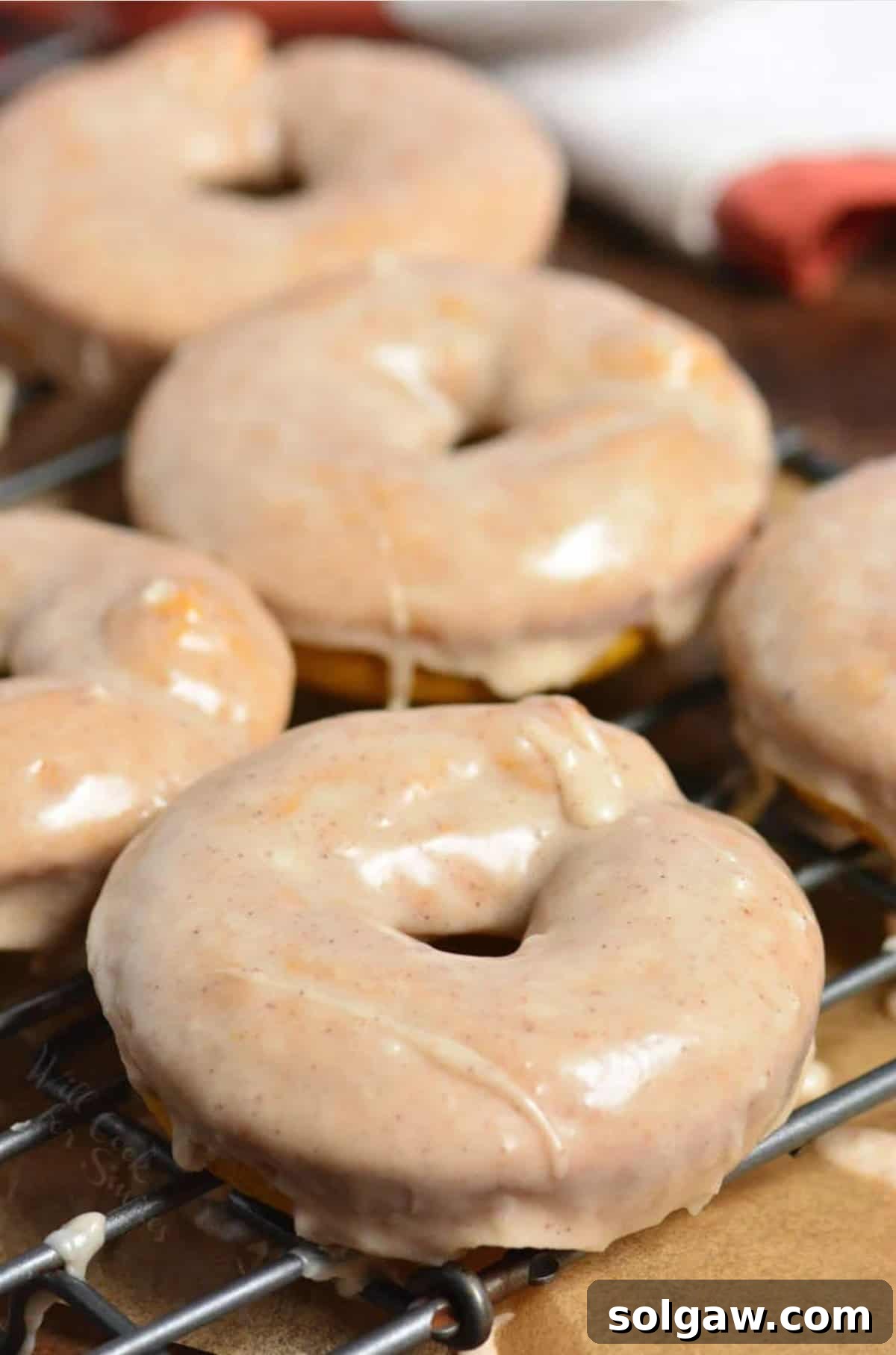 A close-up shot of several pumpkin glazed donuts arranged artfully on a wire rack, emphasizing their appealing texture and shine.