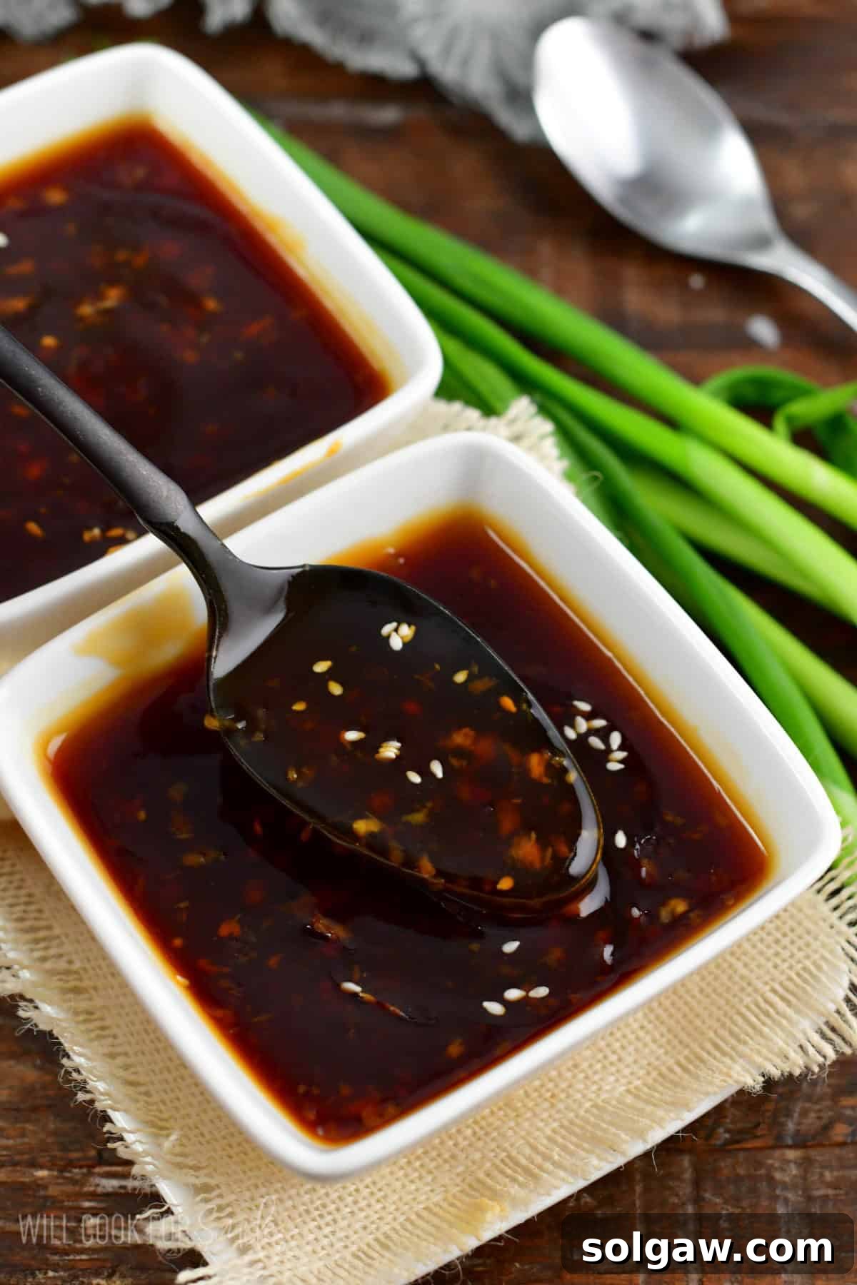 A hand spooning out luscious homemade teriyaki sauce from a pristine white bowl, highlighting its rich, thick consistency.