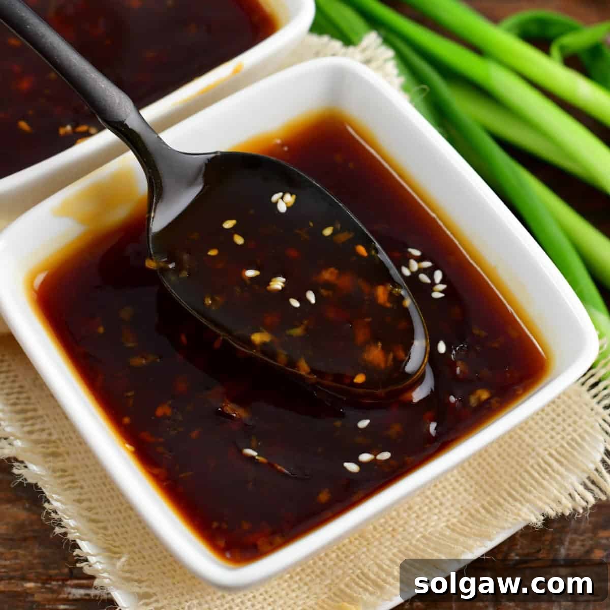 A close-up view of rich, homemade teriyaki sauce being elegantly spooned from a pristine white bowl.